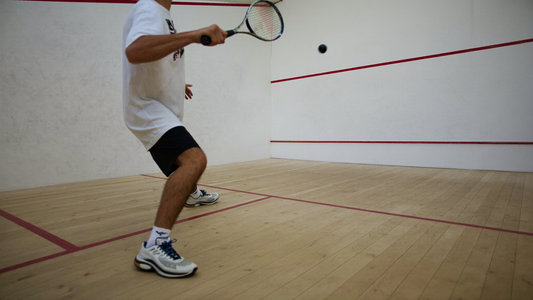 Squashspieler beim Vorhandschlag im Court mit roten Linien an weißer Wand