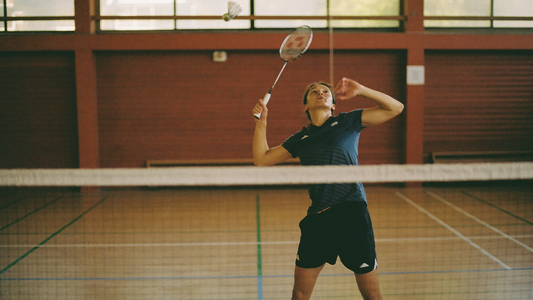 Badmintonspielerin mit erhobenem Schläger und Federball in der Luft am Netz